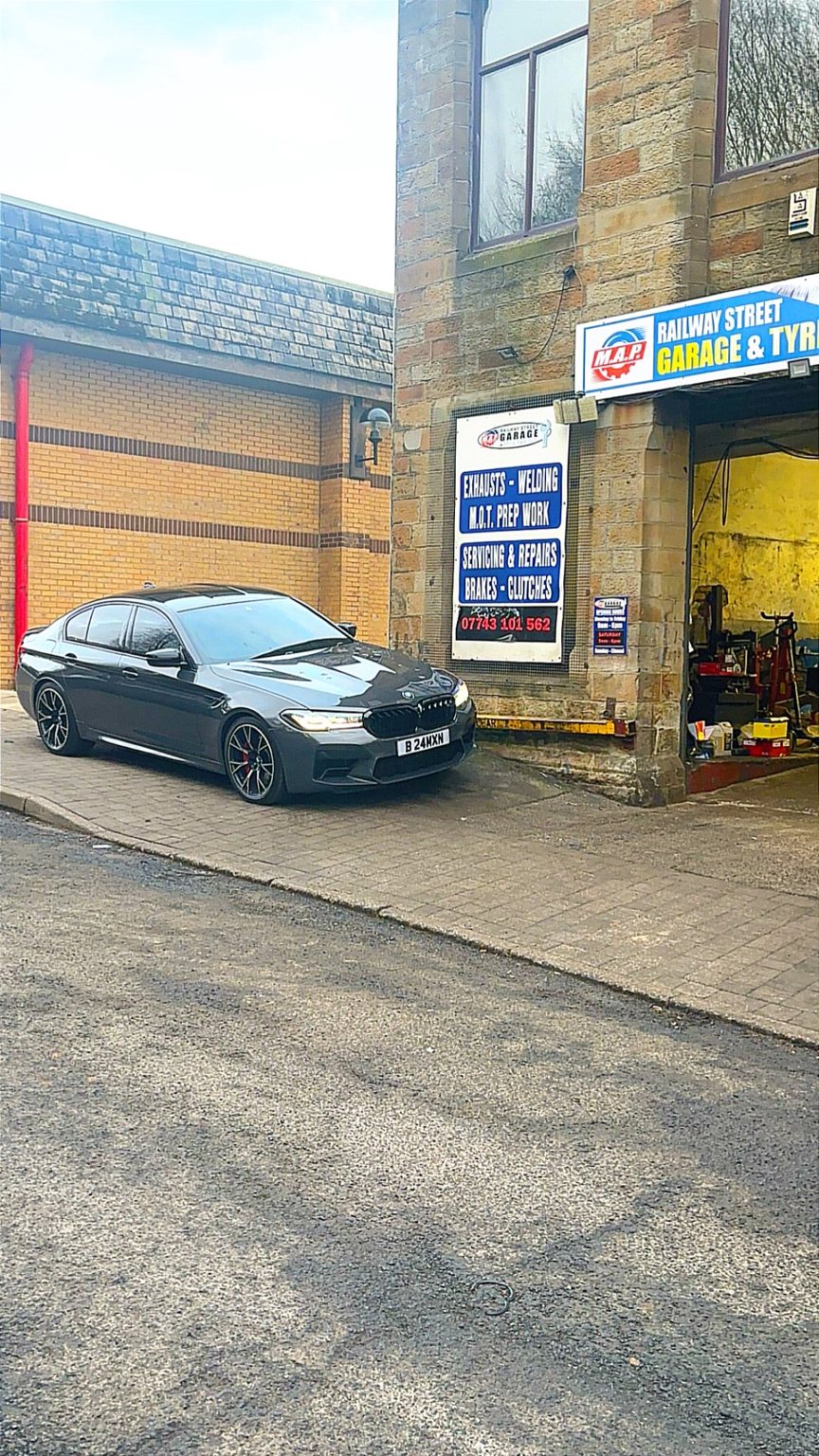 A grey BMW M5 parked on the cobbles outside the workshop, next to the services board and the M.A.P. sign
