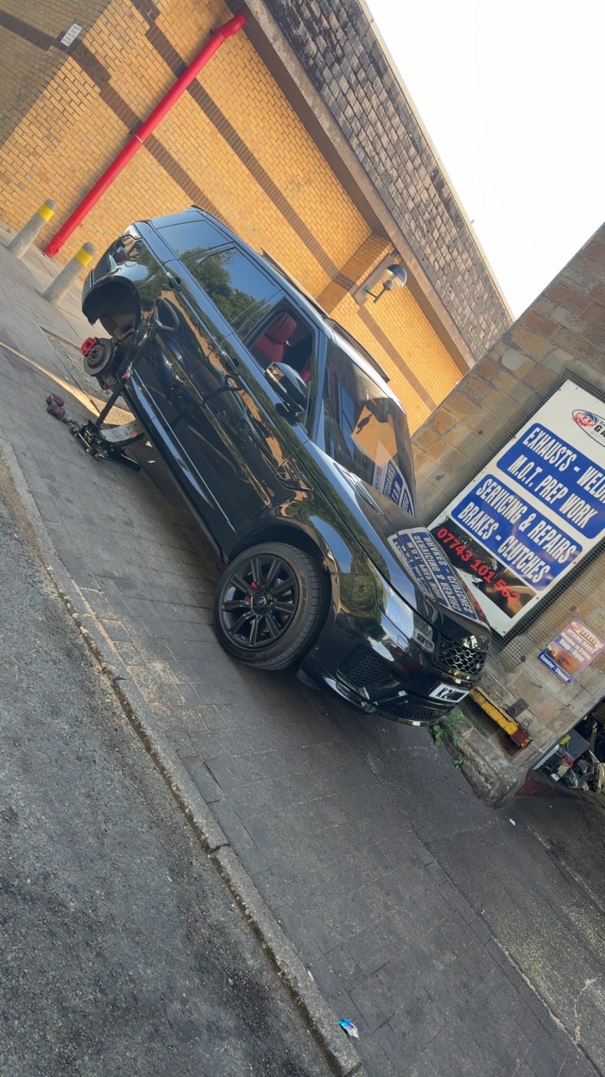 A black Range Rover on a jack outside the garage with a front wheel off and its brakes exposed